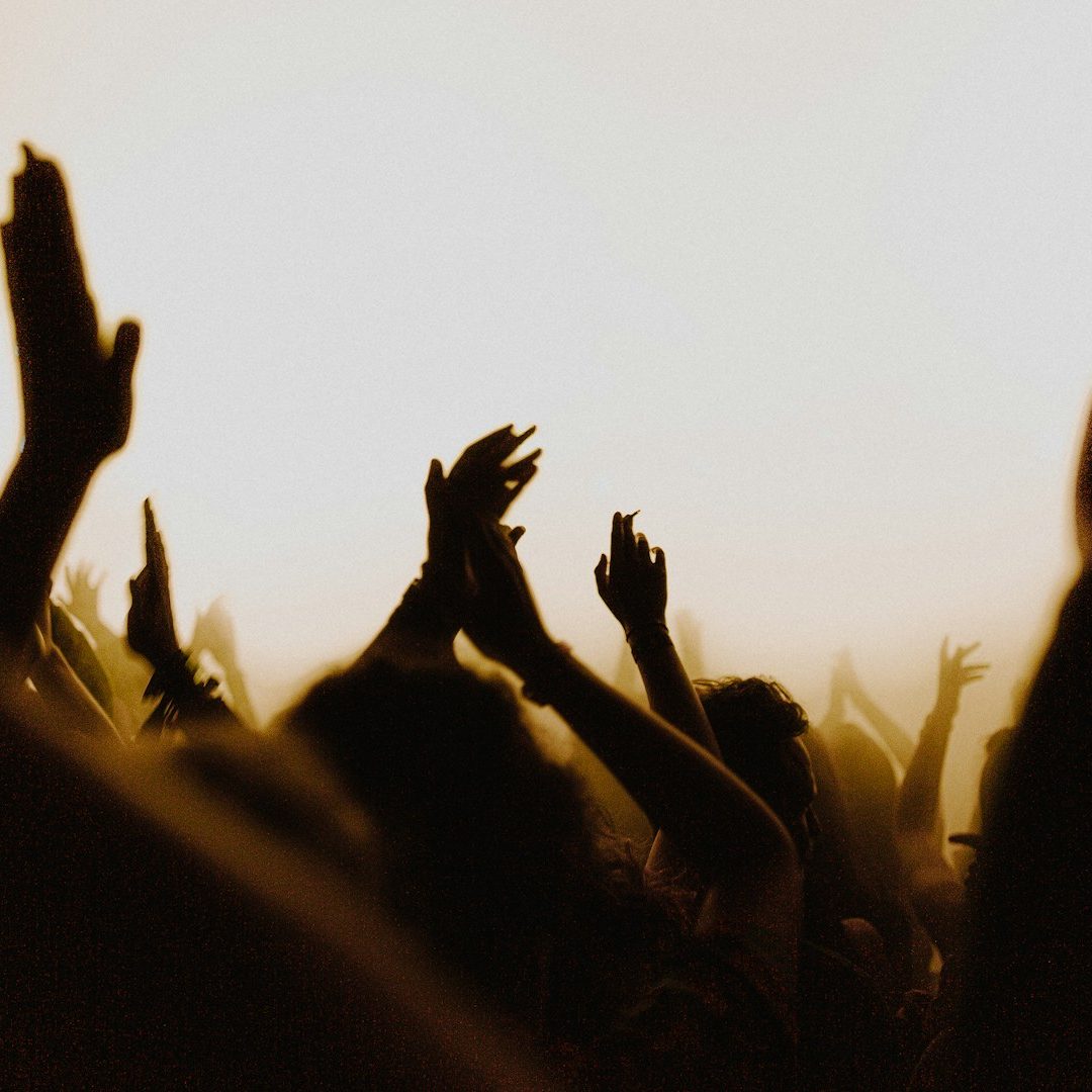 Des silhouettes de bras levés en applaudissements dans une ambiance de concert.